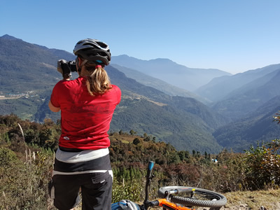 Fotografierende Velofahrerin im Phobjikha-Tal mit Aussicht auf die Berge